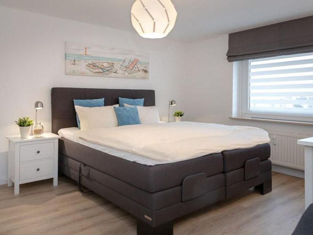 A modern bedroom with a dark-colored bed, white nightstands, a painting on the wall, and a window with blinds.