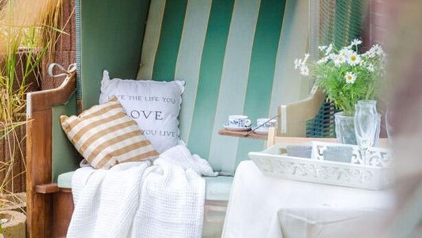 A cozy seating area with a striped pillow, a cushion with a motivational quote, and a small table with a vase of flowers.