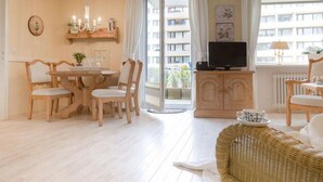 A bright living room with a dining area, wicker furniture, and a television on a cabinet.