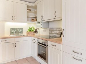 A kitchen with white cabinets, a microwave, and a stove. There is a sign on the wall that says "If you don't like my standards, lower your standards of cooking." - Sylter Residenz - 2-room apartment with terrace (afternoon sun) for 2-4 persons (Sylt)