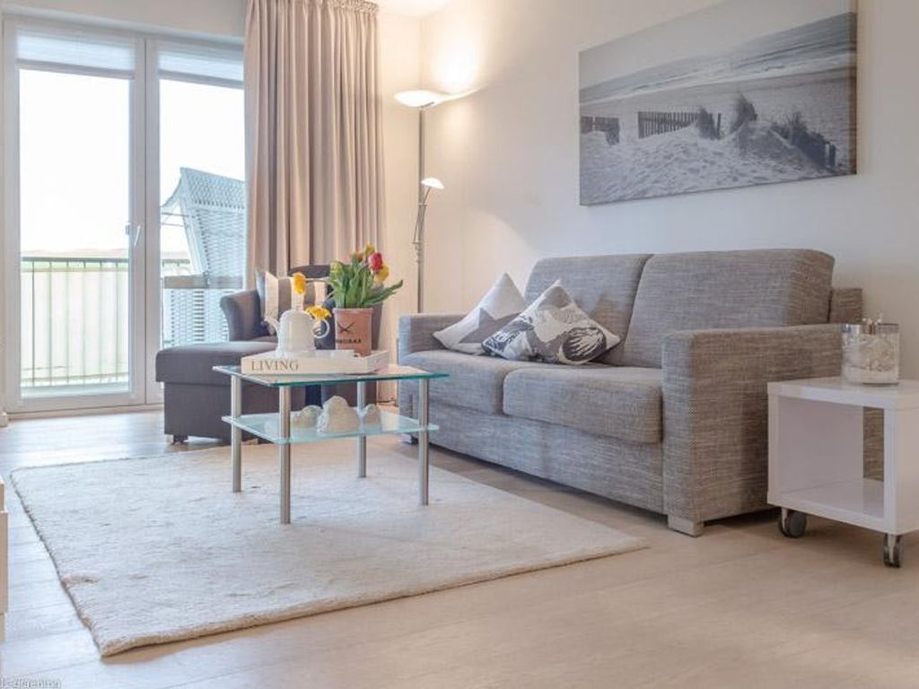 Un salon avec un canapé gris, une table basse en verre, une table d’appoint blanche et un tableau accroché au mur.