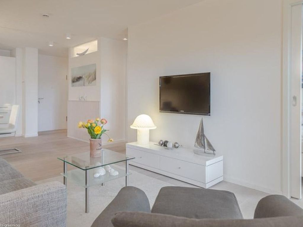 A modern living room with a flat-screen TV mounted on the wall, a glass coffee table, and a white console table with decorative items.
