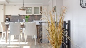 A modern kitchen with white cabinets, a dining area with wicker chairs, and a potted plant. - Big Wave - BIG WAVE maisonette, central, 2 bedrooms, swimming pool, roof terrace, (Sylt)