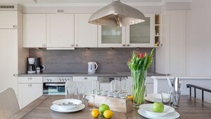 A modern kitchen with white cabinets, a wooden countertop, and a dining area with wicker chairs. - Big Wave - BIG WAVE maisonette, central, 2 bedrooms, swimming pool, roof terrace, (Sylt)