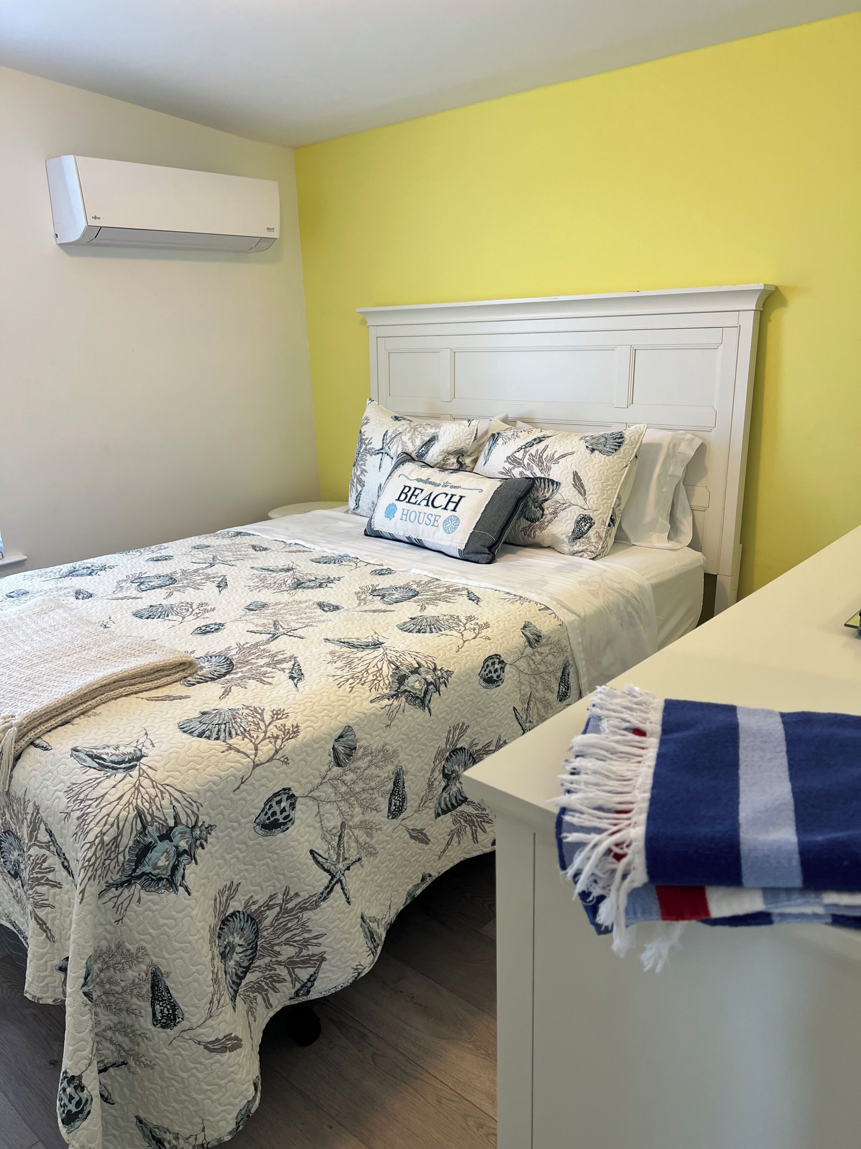 A bedroom with a bed, a bedside table, a nightstand, a wall-mounted air conditioner, and a headboard.