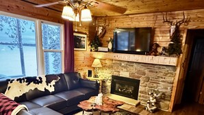 L’intérieur chaleureux d’un chalet avec une cheminée en pierre, un canapé en cuir et un plafond en bois.