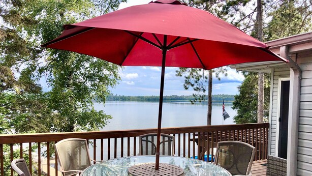Une terrasse avec une table et des chaises en verre, un parasol rouge et une vue sur un lac.