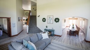 Amplia sala de estar con un sofá gris, una escalera que conduce a otra habitación y un comedor con una mesa larga y sillas.
