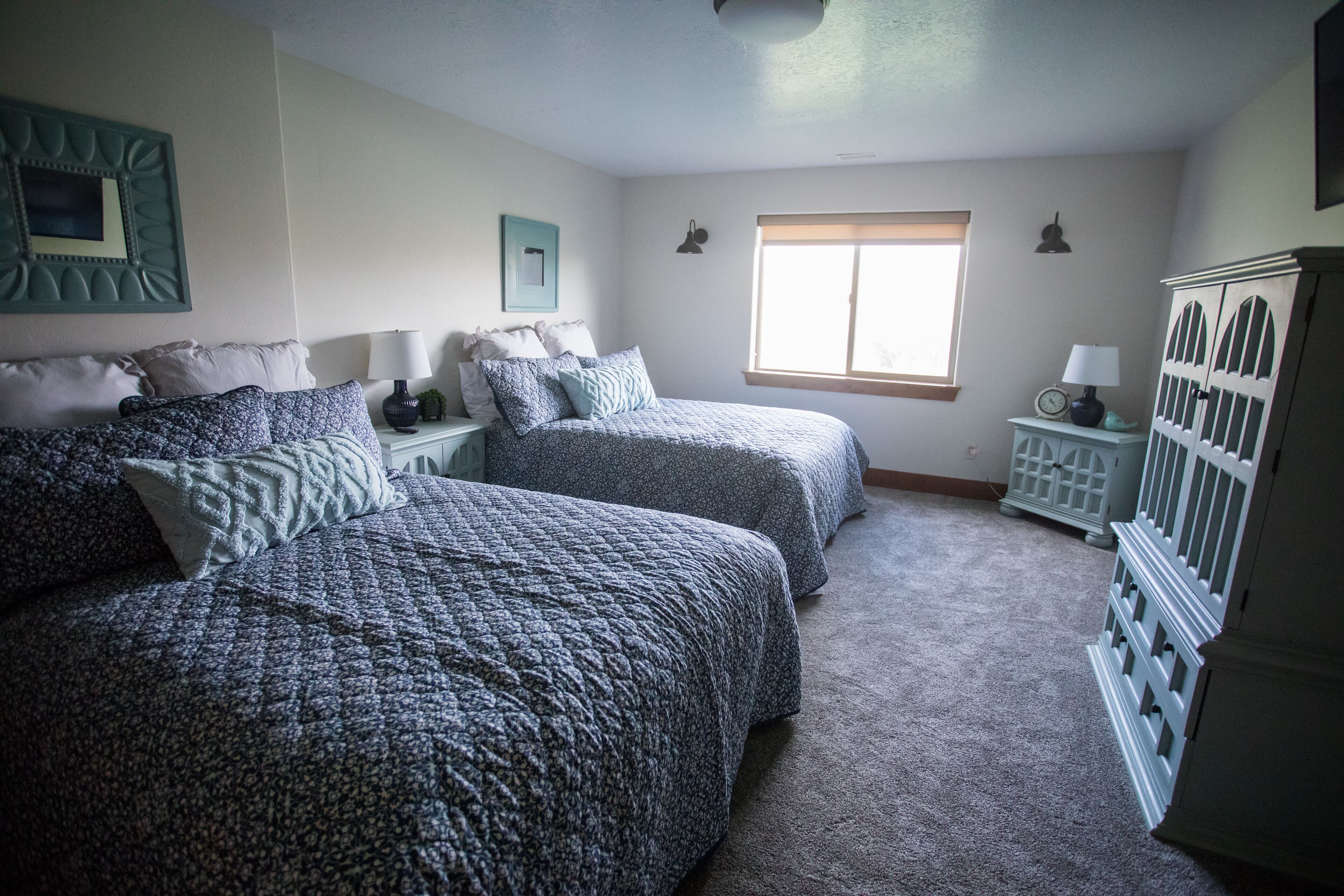 Une chambre avec deux lits, une fenêtre, une commode et une horloge posée sur la commode.