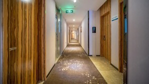 A hotel corridor with wooden paneling on the walls, a carpeted floor, and a sign indicating the direction to the elevator.