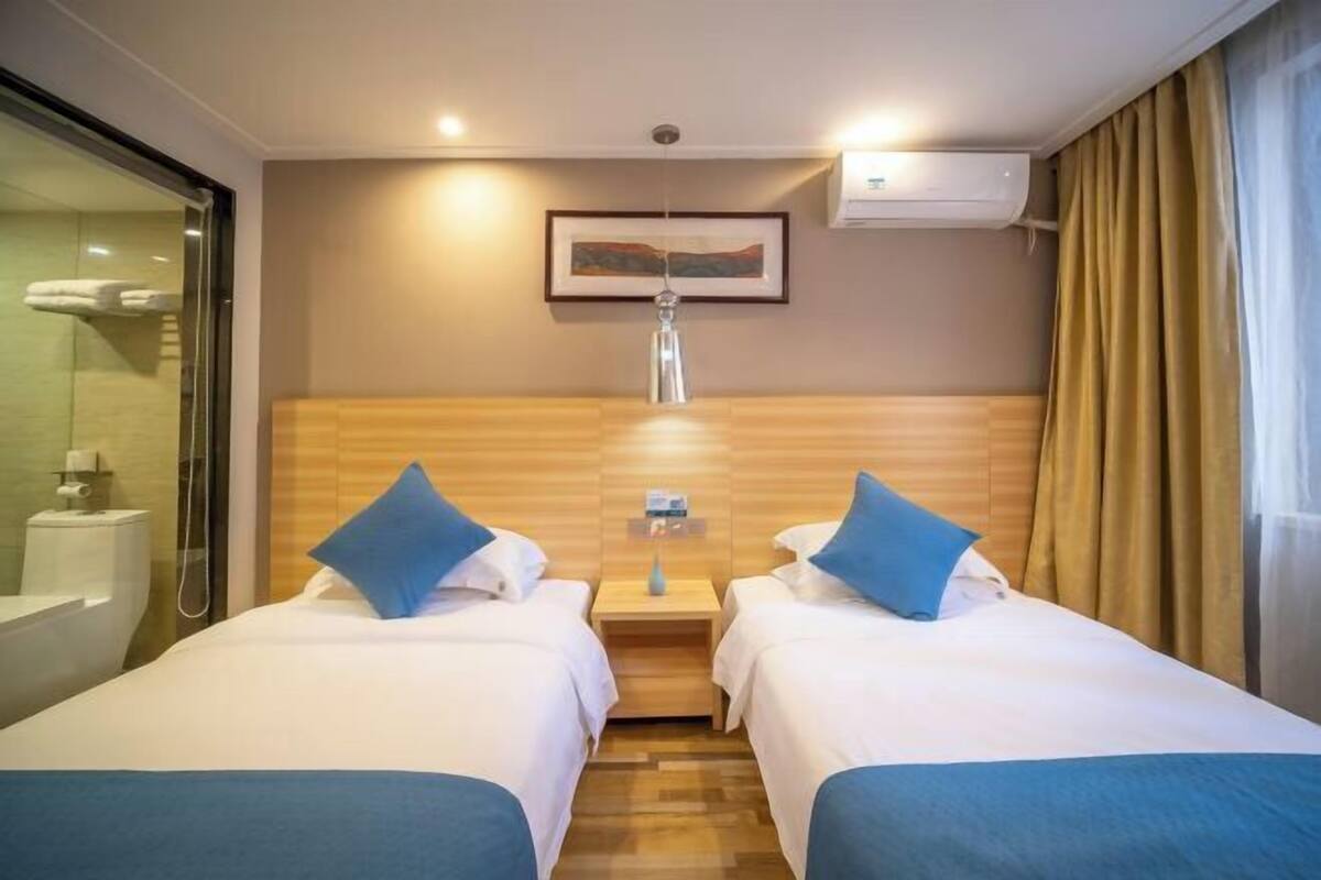 A hotel room with two beds, a shower, a mounted artwork, and an air conditioning unit.