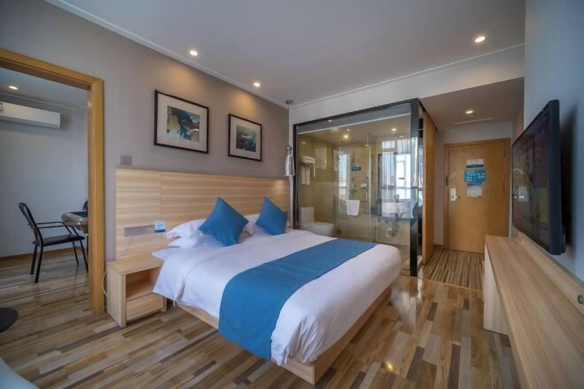 A modern hotel room with a large bed, a desk, a chair, and a TV.