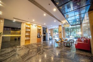 Un vestíbulo de hotel con piso de mármol, un sofá rojo y un muro de cristal.