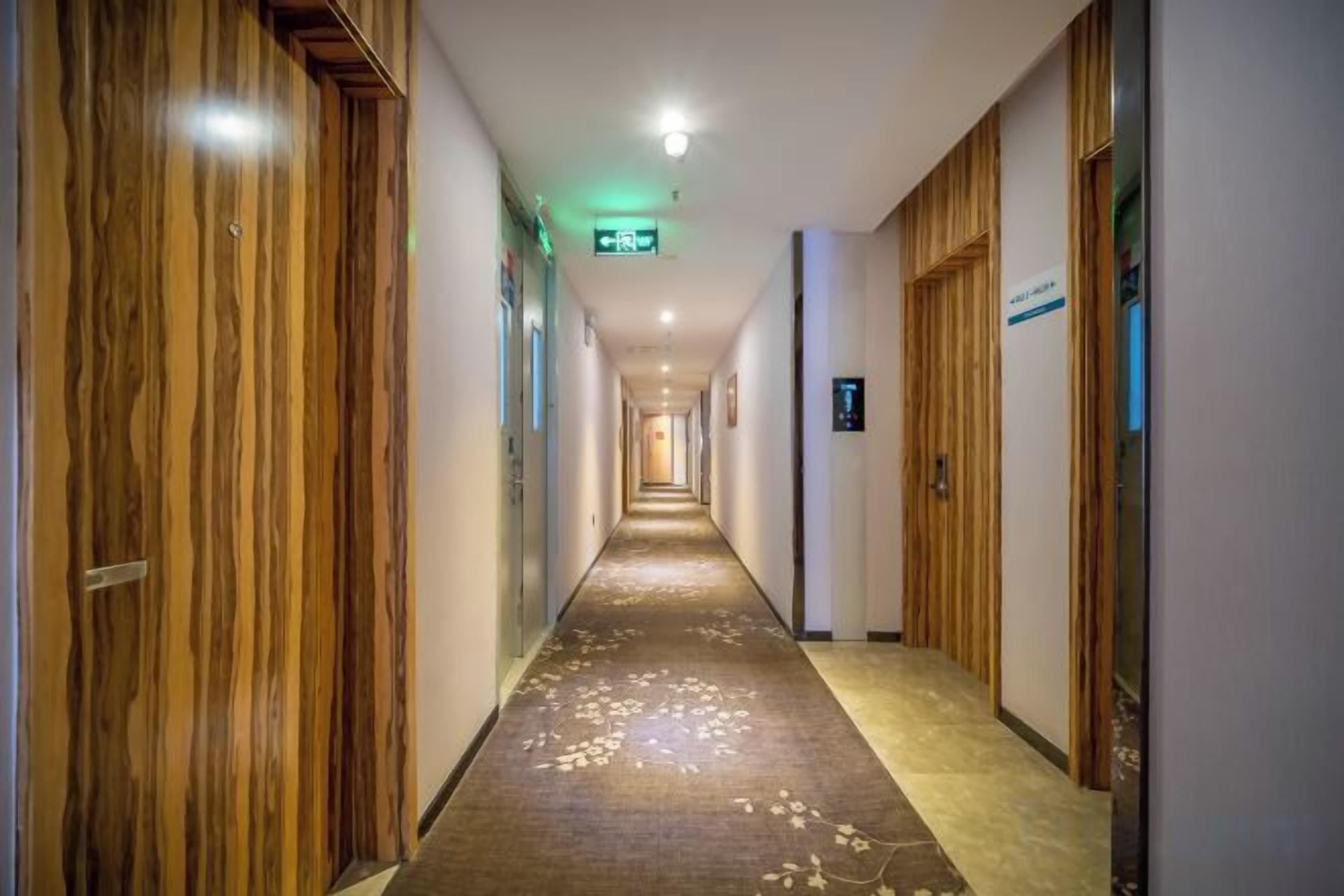 Un couloir d’hôtel avec des portes en bois, un sol recouvert de moquette et un panneau indiquant la direction de l’ascenseur.
