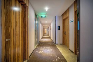 A hotel hallway with wooden doors, a carpeted floor, and a sign indicating the direction to the elevator. - Hengfeng Boutique Hotel (Baise)