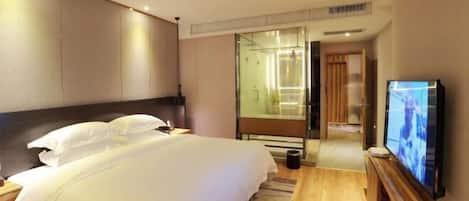 Habitación de hotel con una cama grande, televisión y cabina de ducha de vidrio.