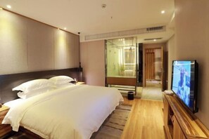 A hotel room with a large bed, a TV, and a glass shower area.