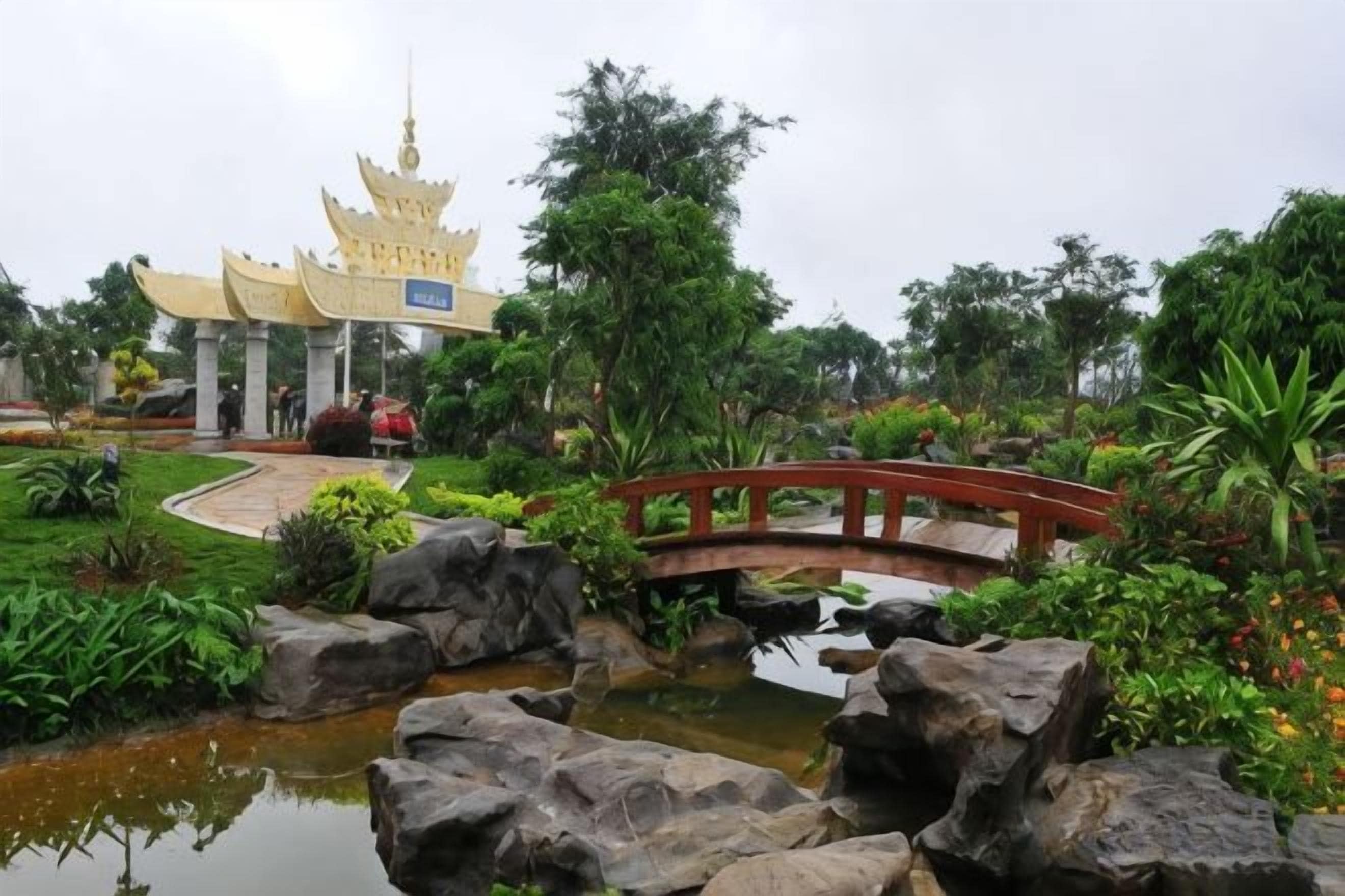 A traditional pagoda-style building with a red bridge over a pond, surrounded by lush greenery.