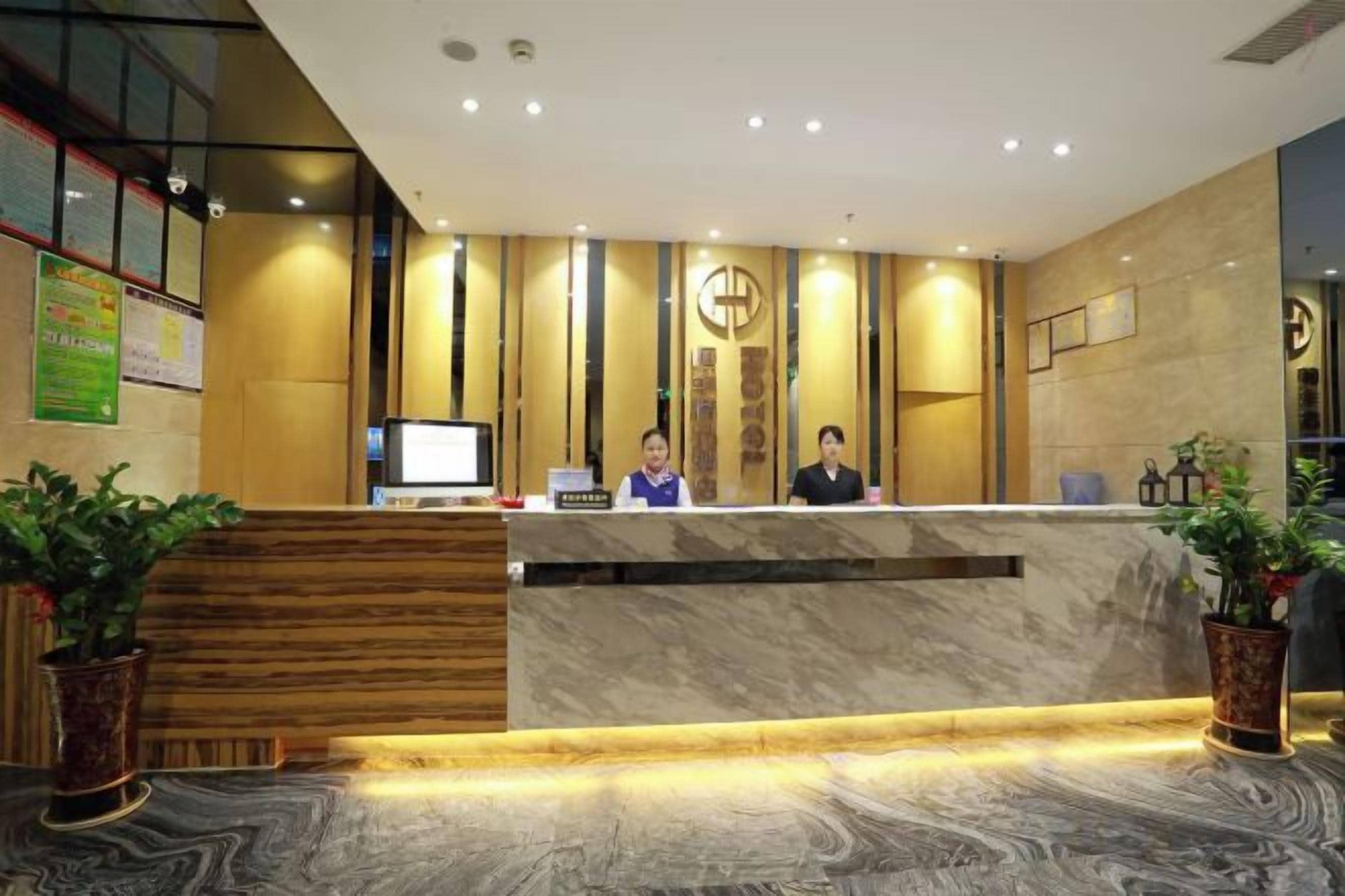 Una recepción de hotel con dos empleados, una pantalla digital y una mesa de recepción.