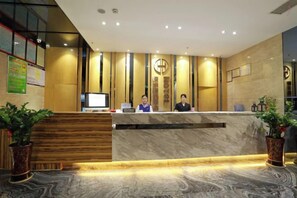 Een hotel receptiebalie met twee medewerkers, een digitaal scherm en een receptiecounter.