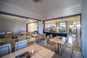 A modern dining area with tables and chairs, a kitchen in the background, and a view of the outdoors. - Hengfeng Boutique Hotel (Baise)