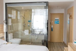 A hotel room with a glass shower enclosure, a bed, a bedside table, and a wooden door. - Hengfeng Boutique Hotel (Baise)