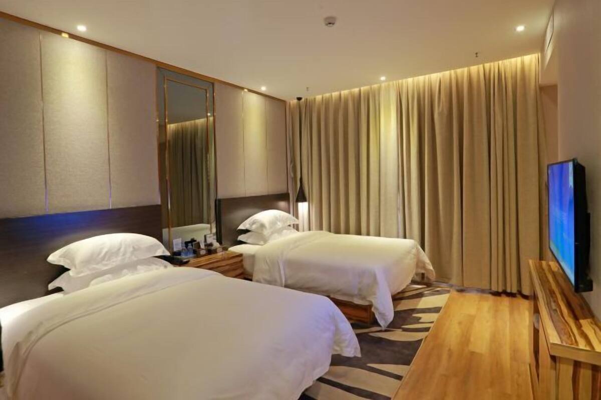 A hotel room with two beds, a TV, a wooden desk, and a large mirror.