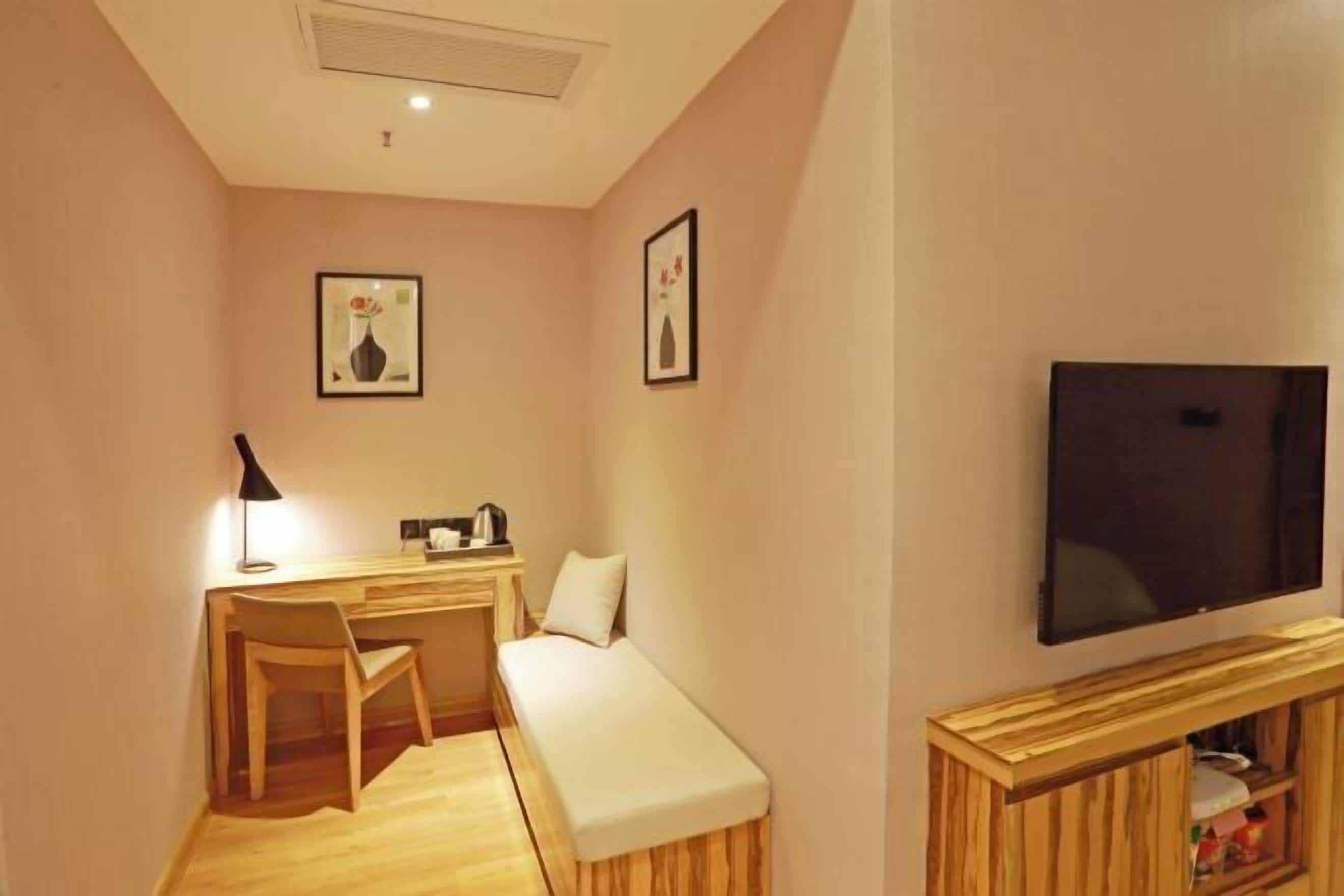 Una habitación compacta con un escritorio de madera, una silla, un banco, un televisor y cuadros en las paredes.