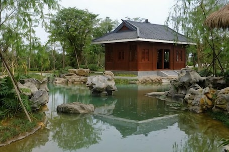A traditional wooden house with a tiled roof, surrounded by a pond with rocks and greenery.. Hengfeng Boutique Hotel
