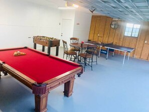 Una sala de billar con mesa de billar, mesa de fútbol de mesa y mesa de ping pong.