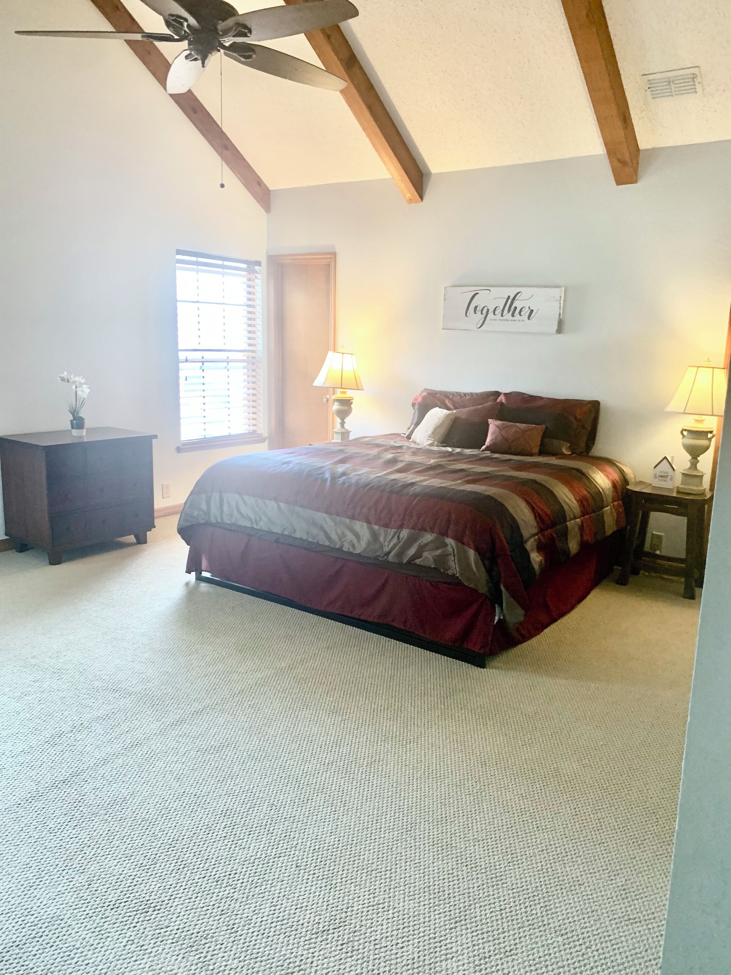 A bedroom with a bed, a nightstand, a dresser, a ceiling fan, and a window with blinds.