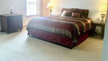 A bedroom with a bed, a nightstand, a dresser, a ceiling fan, and a window with blinds.