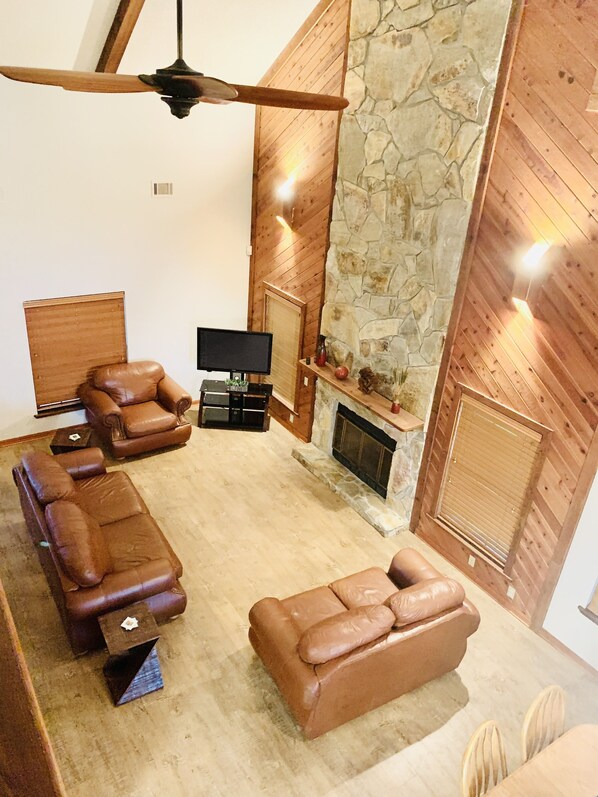 Amplia sala de estar con chimenea de piedra, sofás de cuero y televisor de pantalla plana.