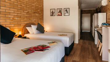 A hotel room with two beds, a brick wall, and a hallway leading to a kitchenette.