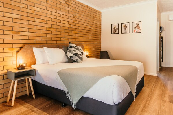 A modern bedroom with a brick-patterned headboard, a neatly made bed with a grey and white color scheme, and a small bedside table with a lamp. - Oasis Motor Inn Blackall (Blackall)