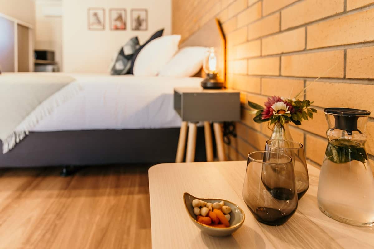 A hotel room with a bed, a bedside table with a vase of flowers, a pitcher, and glasses.