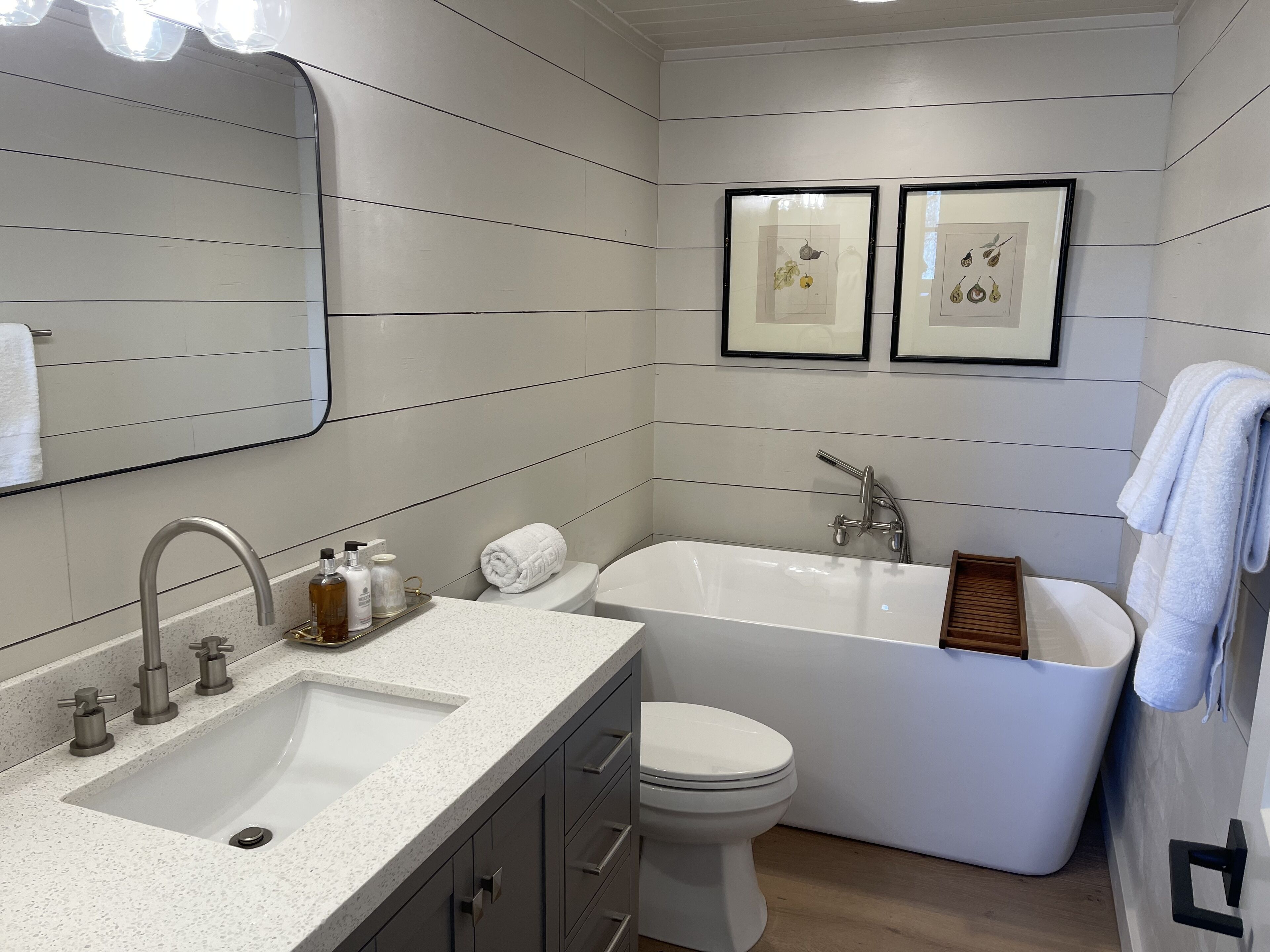 Ein modernes Badezimmer mit einer freistehenden Badewanne, einem Waschbecken inklusive Spiegel und zwei gerahmten Pflanzenmotiven an der Wand.