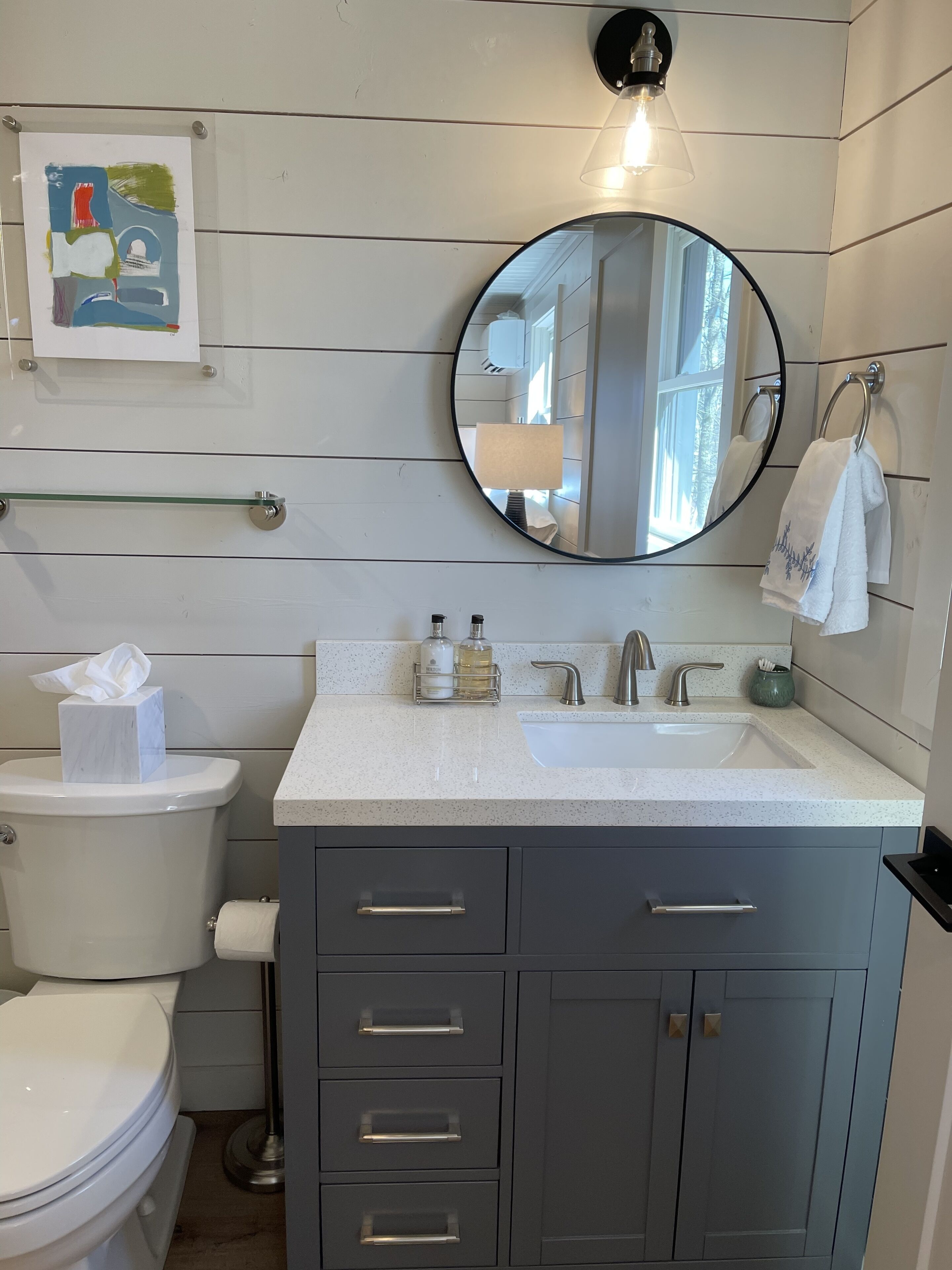 A bathroom with a white toilet, a sink with a mirror above it, and a vanity with drawers and a cabinet.