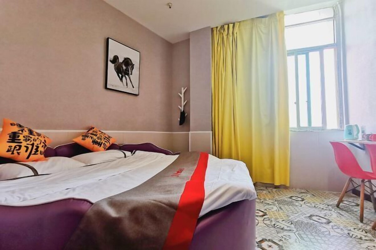 Habitación de hotel con una cama, una silla, una ventana con cortinas amarillas, un cuadro en la pared y una cornamenta decorativa.