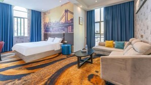 Een hotelkamer met een bed, een bank, een salontafel en een groot raam met gordijnen.