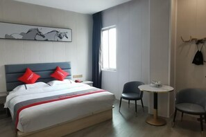 A hotel room with a bed, a small round table, two chairs, a window with curtains, and a wall-mounted artwork.