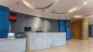Een hotel receptie met een marmeren balie, een digitaal scherm en een rood bord met daarop een nooduitgang.