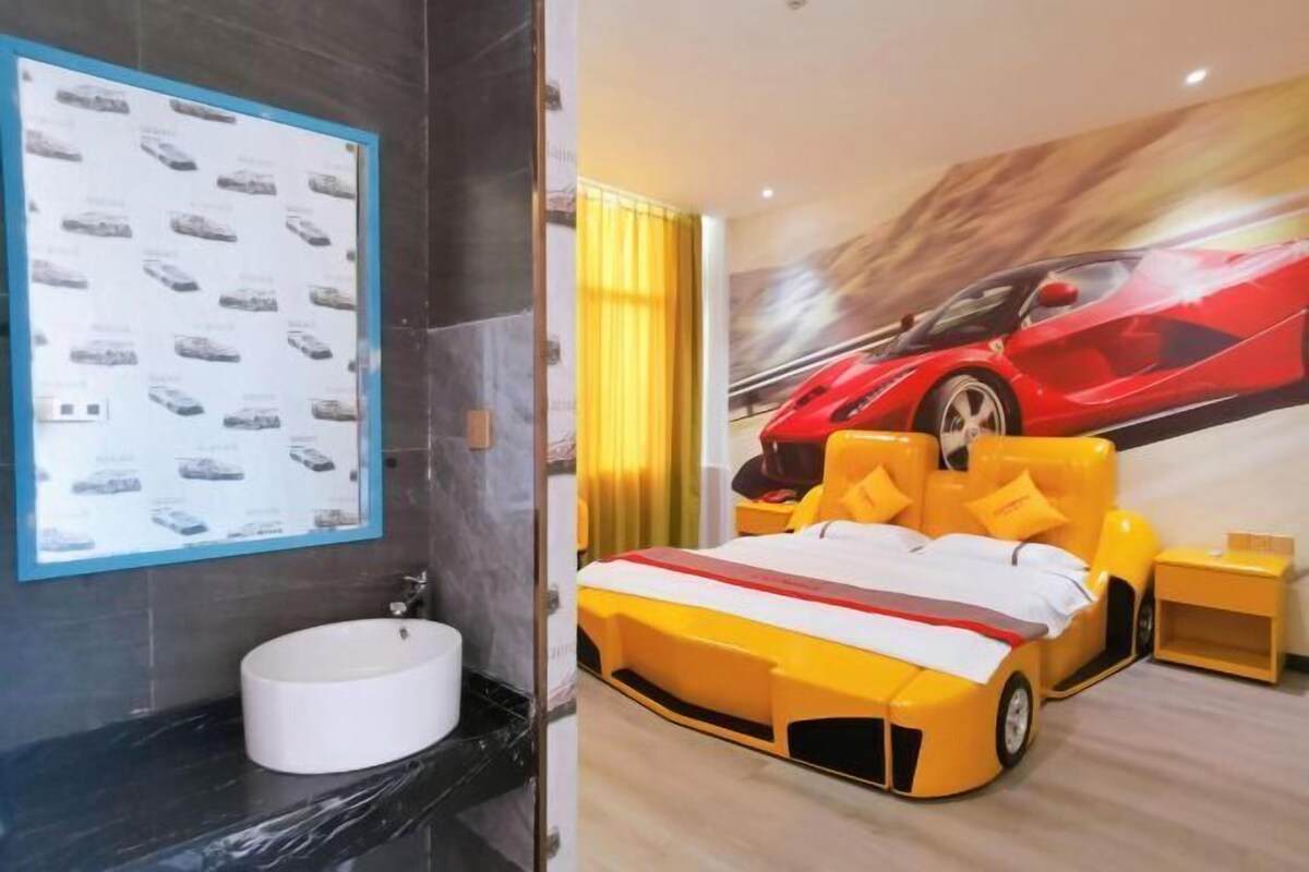Un dormitorio moderno con una cama diseñada como un coche deportivo, un cartel grande de un coche deportivo rojo y un baño con encimera y lavabo de mármol.