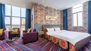 Een hotelkamer met een groot bed, een accentmuur van steen, uitzicht door het raam en een kleurrijk gestreept tapijt.