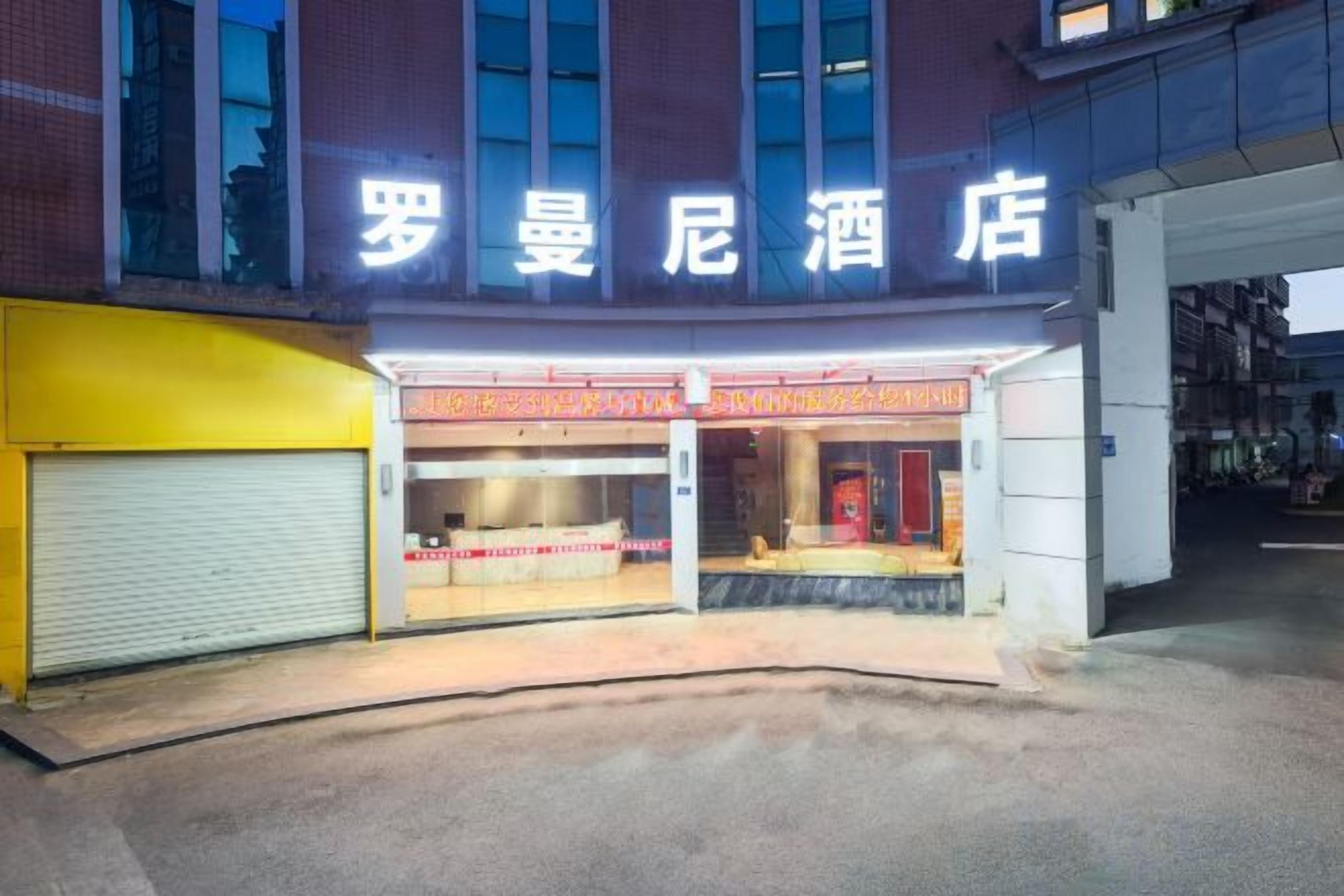 A hotel entrance with a neon sign, a closed garage door, and a storefront with a red awning.