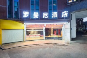 A hotel entrance with a neon sign, a closed garage door, and a storefront with a red awning. - Roman Hotel (Jian'ou)