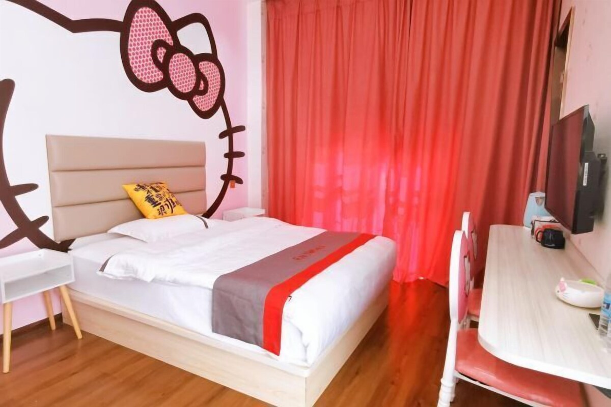 Una habitación de hotel con cama, escritorio, silla, televisor y una decoración de pared de Hello Kitty.