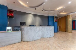 Un'area reception di un hotel con un bancone in marmo, un display digitale e un arredamento moderno.