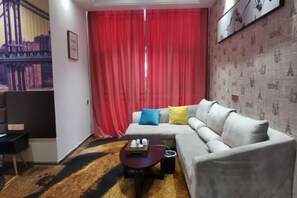 Una sala de estar moderna con un sofá gris, cortinas rojas y una alfombra estampada.