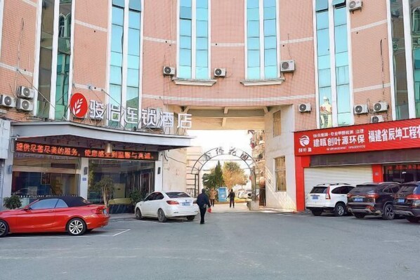 A building with a large sign above the entrance, a parking lot with several cars, and a few people walking in front.
